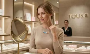 Mujer sonriente admira su collar Tous con ositos de colores, incluyendo un verde vibrante, frente a un espejo en una joyería.