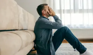 Mężczyzna siedzi na podłodze, zakrywając twarz dłońmi. Czy to kryzys wieku średniego u męża co robić?