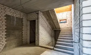 Schody prowadzące do piwnicy, gdzie planowana jest wentylacja wilgotnej piwnicy. Betonowe schody, ściany z białej cegły, sufit.