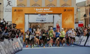 Biegacze startują w maratonie. Wielka brama z napisem "Cracovia Maraton" i hasłem "Masz moc!" symbolizuje wyzwanie, ile ma maraton.