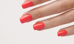 Main d'une femme avec un vernis corail vif, parfait pour un ongle vacances.