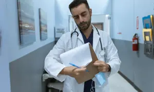 Lekarz w białym kitlu z notatnikiem i długopisem w szpitalnym korytarzu.