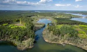 Malownicze jeziora i lasy tworzą krajobraz pojezierza brodnickiego. Woda odbija błękitne niebo z białymi chmurami.