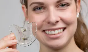 Uśmiechnięta dziewczyna trzyma aparat ruchomy. Czy aparat ruchomy wyprostuje zęby?