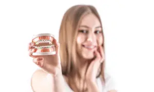 Uśmiechnięta dziewczyna prezentuje model szczęki z kolorowymi pierścieniami ortodontycznymi na zębach.