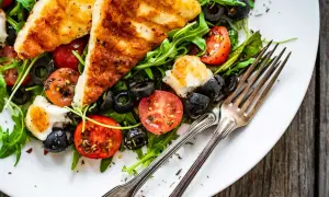 Pyszna sałatka z grillowanym halloumi, pomidorkami koktajlowymi i czarnymi oliwkami na rukoli. Idealna na lekki posiłek.