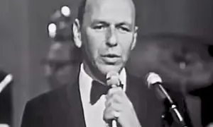 Frank Sinatra śpiewa "Fly Me to the Moon lyrics", ubrany w smoking.