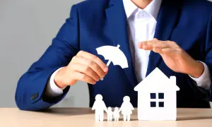 Mężczyzna w garniturze symbolizuje ubezpieczenie spłaty kredytu, chroniąc dom i rodzinę parasolką.