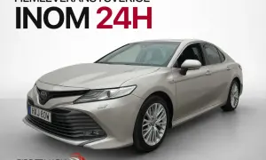 En silverfärgad, begagnad Toyota Camry hybrid visas framifrån. Hemleverans inom 24 timmar i Sverige.