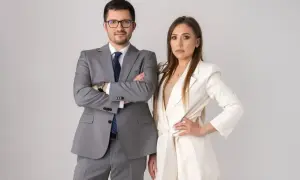 Para prawników w garniturach, mężczyzna w szarym, kobieta w białym, na jasnym tle.