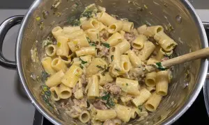 Rigatoni mit cremiger Sauce, Fenchel und Salsiccia. Ein Holzlöffel rührt die köstliche Pasta in einem Topf.