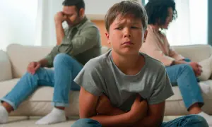 Bambino triste in primo piano, con i genitori separati seduti alle sue spalle, voltati l'uno dall'altra.