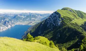 Panoramica mozzafiato dal Monte Baldo: lago blu intenso, montagne verdi e un cielo limpido.