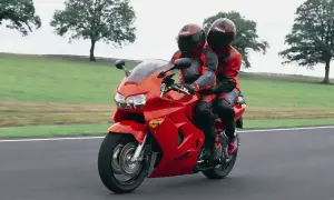Dwie osoby w czerwonych kombinezonach jadą na czerwonym motocyklu Honda VFR 800.