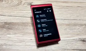 Czerwony translator głosowy Vasco na drewnianym blacie. Urządzenie oferuje tłumaczenie mowy, rozmów telefonicznych, zdjęć i tekstu.