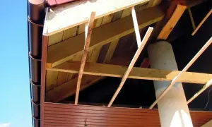 Widok od spodu na konstrukcję dachu z widoczną podprzybitką, rynną i kominem.