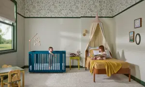 A teal crib offers bold crib color ideas in a nursery with whimsical wallpaper. Two children enjoy the room.