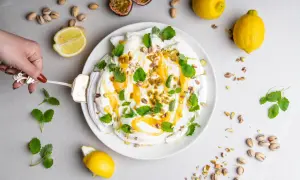 En hand skär en pavlova med lemon curd, toppad med passionsfrukt, pistagenötter och mynta.