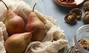 Trzy rumiane gruszki na białym materiale, obok orzechy i słoik z ciasteczkami. Czy gruszki są zdrowe? Tak, to pyszny i zdrowy owoc!