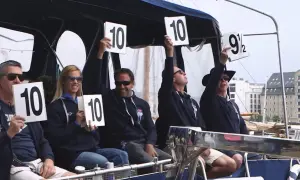 A group of diving judges hold up scorecards. Most show a perfect 10, but one judge holds up a 9.5.