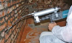 Gerät zur nachträglichen **Verkieselung Mauerwerk selber machen**. Ein Mann injiziert eine Flüssigkeit in eine Ziegelwand.
