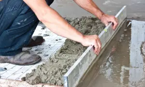 Ręce budowlańca wyrównują świeżą wylewkę betonową na zewnątrz za pomocą łaty.