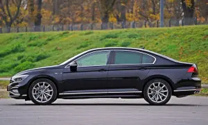 Elegancki, czarny sedan z chromowanymi detalami stoi na tle jesiennego krajobrazu.