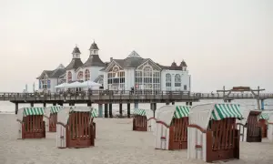 Plaża w Stralsundzie w Niemczech z charakterystycznymi koszami plażowymi i molo z białą budowlą.