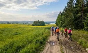 Grupa rowerzystów przemierza malownicze **olsztyńskie trasy rowerowe** wśród pól rzepaku i lasów.