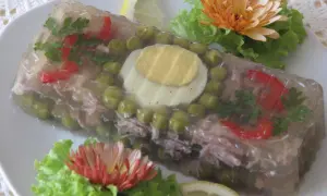 Pyszna galareta z golonki z groszkiem, papryką, jajkiem i natką pietruszki, ozdobiona kwiatami i cytryną.