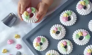 Dziecko ozdabia okrągłe mini bezy kolorowymi kleksami z kremu. Obok leży końcówka do szprycowania.