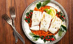 Gedünsteter Fisch auf Tomatenragout, festlich dekoriert mit Beeren und Tannenzweigen. Ein Gericht, das an italienische Weihnachtsrezepte erinnert.