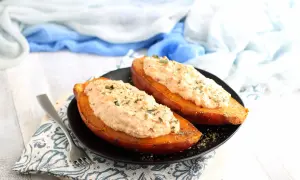 Due patate dolci al forno, tagliate a metà e farcite con un cremoso ripieno, guarnite con erbe aromatiche.