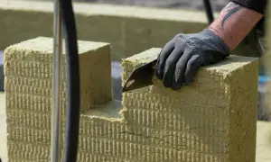 Ręka w rękawicy tnie piłą wełnę skalną 10. Materiał izolacyjny jest przygotowywany do montażu.