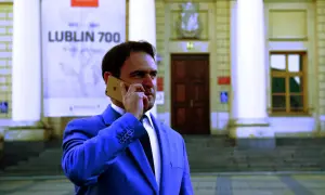 Mężczyzna w garniturze rozmawia przez telefon przed budynkiem z napisem "Lublin 700". Czy adwokat z urzędu jest płatny?