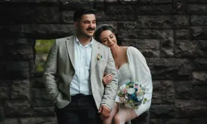 Para młoda w dniu ślubu, ona opiera głowę na jego ramieniu, trzyma bukiet.