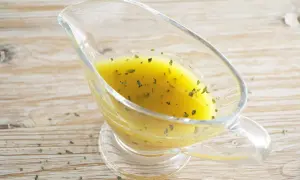 Salsa dorada con hierbas verdes en una salsera de cristal. Perfecta vinagreta de mostaza para realzar tus platos.