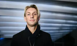Anders Hansen, din personlighet speglas i blicken. En man med karisma, klädd i svart jacka och scarf, mot en bakgrund av horisontella linjer.