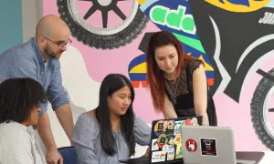 Apprendre comment devenir un développeur web avec des collègues devant un mur coloré.