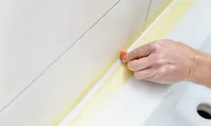 Dłoń wygładza świeży silikon na taśmie, odpowiadając na pytanie, czy na stary silikon można położyć nowy.