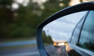 Specchietto retrovisore con indicatore del sistema side assist attivo, riflette la strada e le luci delle auto.