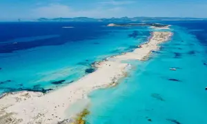 Arena blanca y aguas turquesas en la mejor playa de Formentera. Un paraíso con barcos y gente disfrutando del sol.