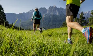 Zwei Läufer genießen das Zugspitze Laufen auf einer grünen Wiese vor majestätischen Bergen.