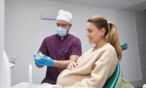Dentysta wyjaśnia ciężarnej pacjentce procedurę leczenia kanałowego, pokazując model zębów.