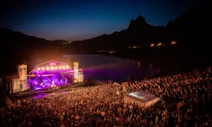 Gran concierto nocturno en el Pirineos Sur. Un mar de gente disfruta de la música bajo un cielo estrellado y montañas.
