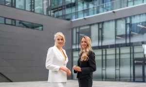 Dwie kobiety w garniturach stoją przed nowoczesnym budynkiem biurowym.