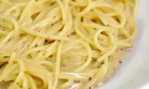En närbild på en krämig portion spaghetti cacio e pepe, med synliga pepparkorn i den lena såsen.