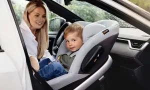 Uśmiechnięta mama patrzy na synka w foteliku na przednim siedzeniu. Czy dziecko może jechać w foteliku na przednim siedzeniu? Tak, jeśli jest odpowiednio zabezpieczone.