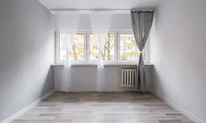 Biały karnisz sufitowy zamontowany nad oknem, na którym wiszą zwiewne firanki i zasłona.