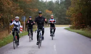 Peleton kolarzy jedzie drogą wśród jesiennych drzew. Czy to wyścig, czy wspólna przejażdżka?